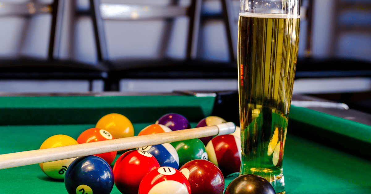 A set of billiard balls, cue and a glass of beer