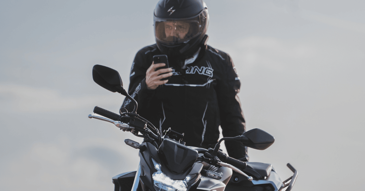 Geared motorcyclist standing next to his motorcycle and looking at his phone